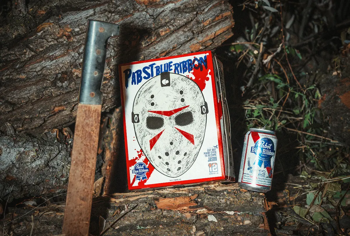A Pabst Blue Ribbon Jason Voorhees mask 12-pack and can beside a machete